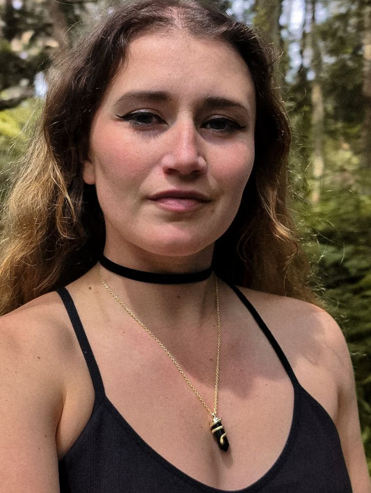 Woman wearing a black tank top and gold necklace with a forest background