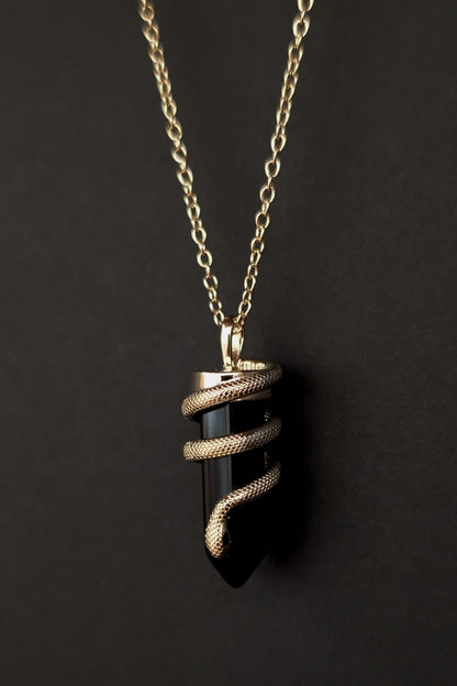 Necklace with a black pendant and gold chain on a dark background