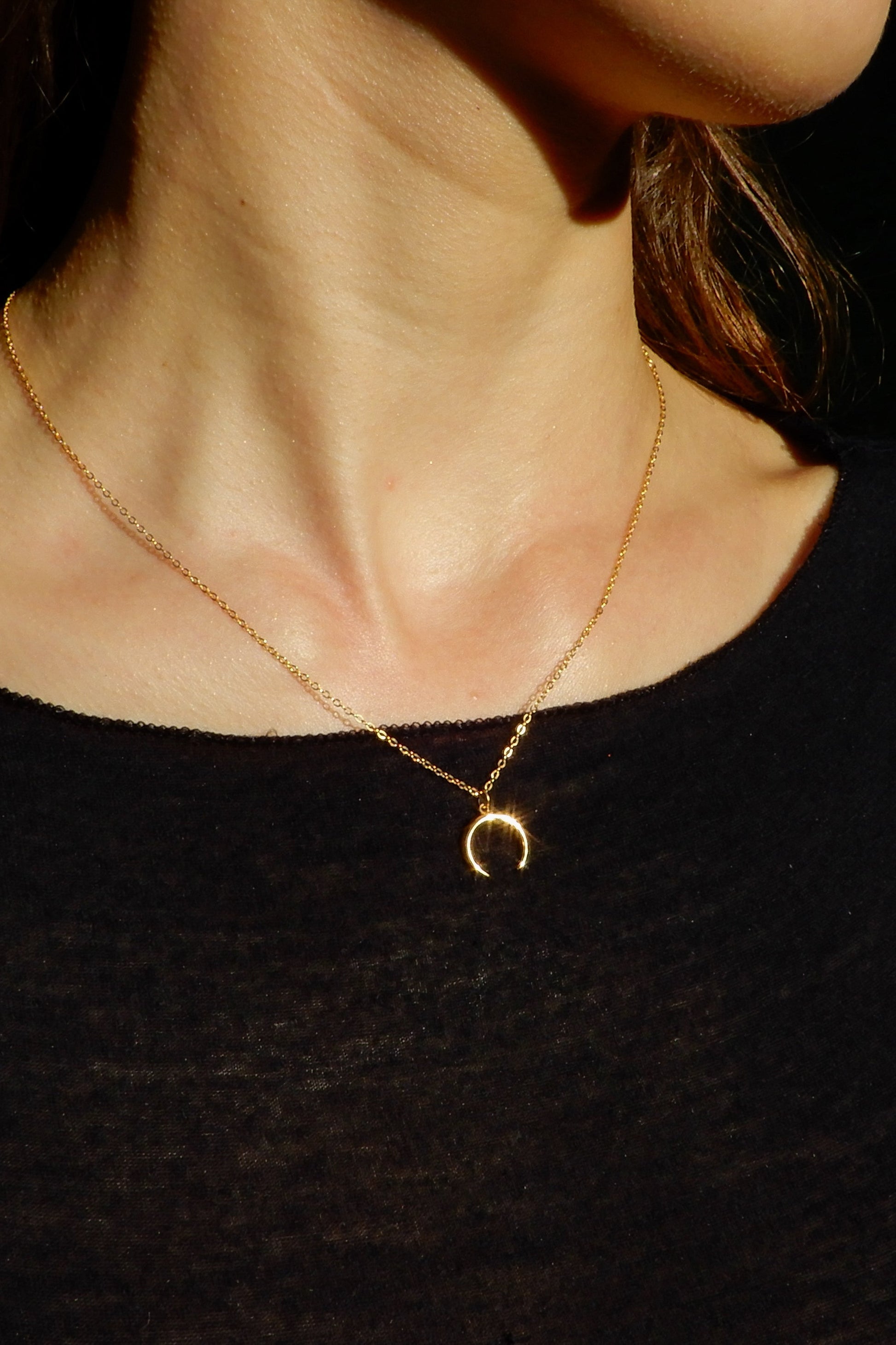 Person wearing a gold necklace with a crescent moon pendant against a dark background